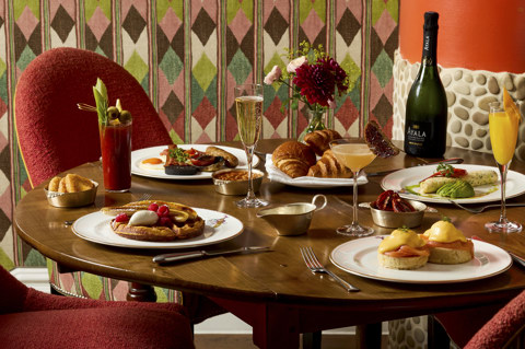A landscape image of multiple dishes from the New Years Day Brunch menu at Refuel, The Soho Hotel. There are also glasses of champagne and themed cocktails.