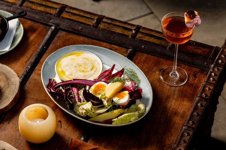A selection of fire-cooked dishes and cocktails sit on a wooden coffee table