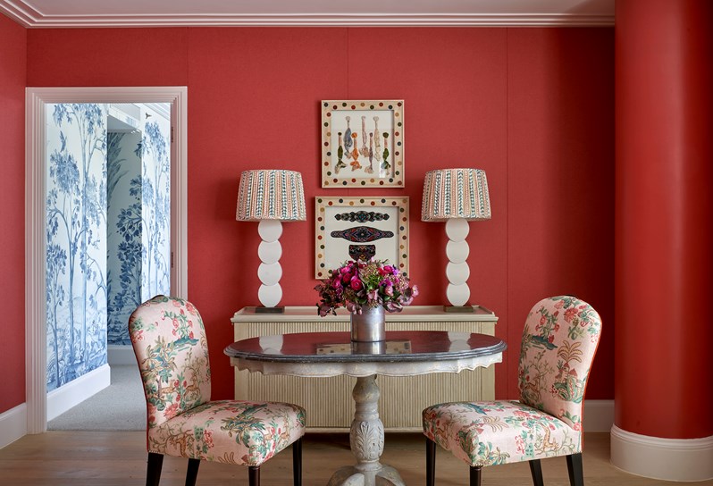 A dining table with two pink patterned dining chairs with a wooden console table and two white lamps with patterned shades