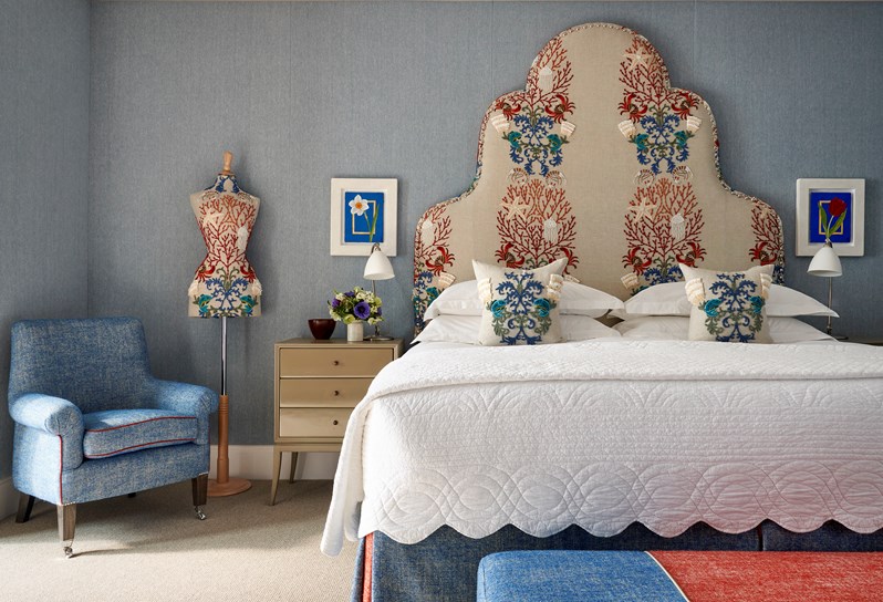 A bedroom featuring a blue double bed with a headboard upholstered in a sea life motif which matches a mannequin to the left, there is a red an blue footstall at the end of the bed.