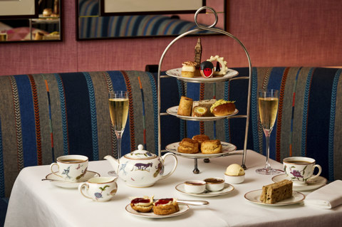 An afternoon tea stand set up at Brumus in Haymarket Hotel. There cakes are designed to reflect iconic London landmarks, scones and sandwiches and cups of tea and glasses of Champagne