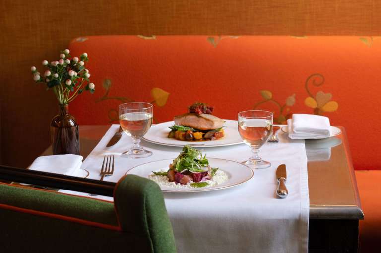 A wide angle shot of a table set up for dinner at The Crosby Bar: there are dishes of salmon and the beetroot salad, with white wine pairings