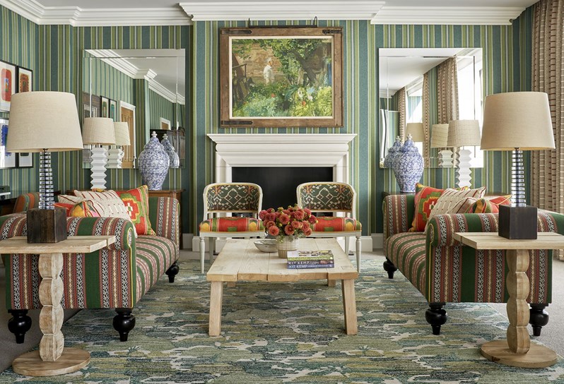 Shot of the living room in a One Bedroom Suite at the Crosby Street Hotel facing a fire place and two chairs in front, a coffee table and on the side two sofas with each two tables on either side and lamps on top