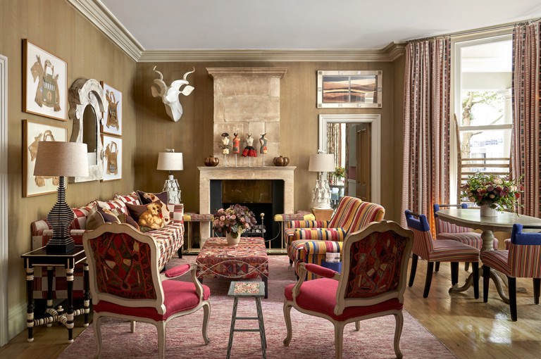 Wide shot of the Drawing Room at Knightsbridge Hotel, the room displays a sofa on the left, in the foreground the backs of two arm chairs that face into the room. in the centre a low embroidered coffee table, on the right hand side of the seating area, two striped arm chairs. On the fart right of the image we see a round dining table with 4 striped chairs around it.