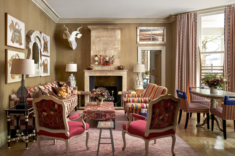 Wide shot of the Drawing Room at Knightsbridge Hotel, the room displays a sofa on the left, in the foreground the backs of two arm chairs that face into the room. in the centre a low embroidered coffee table, on the right hand side of the seating area, two striped arm chairs. On the fart right of the image we see a round dining table with 4 striped chairs around it.  