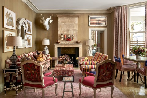 Wide shot of the Drawing Room at Knightsbridge Hotel, the room displays a sofa on the left, in the foreground the backs of two arm chairs that face into the room. in the centre a low embroidered coffee table, on the right hand side of the seating area, two striped arm chairs. On the fart right of the image we see a round dining table with 4 striped chairs around it.