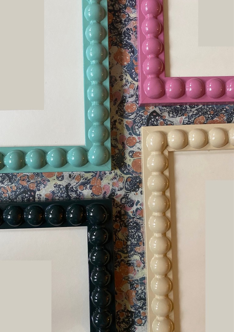 A close up shot of the corners of four different coloured bobbin frames by Domenica Marland laid on a marble background
