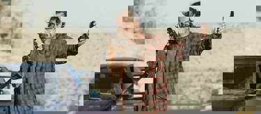 Still from One Battle After Another. A frantic looking man stands in a desert landscape, pointing a large gun ahead of him