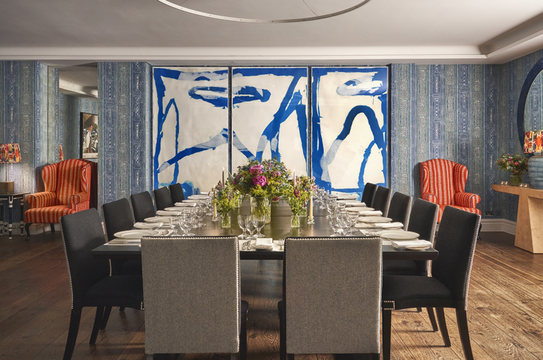 An straight on image of the long dining table set up in the Indigo Room, there are floral bouquets in the centre and candles. each place around the table has a placemat, plate, cutlery, glassware and napkins ready for dining. private events room at The Soho Hotel.