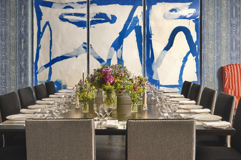 An straight on image of the long dining table set up in the Indigo Room, there are floral bouquets in the centre and candles. each place around the table has a placemat, plate, cutlery, glassware and napkins ready for dining. private events room at The Soho Hotel.