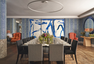 An straight on image of the long dining table set up in the Indigo Room, there are floral bouquets in the centre and candles. each place around the table has a placemat, plate, cutlery, glassware and napkins ready for dining. private events room at The Soho Hotel.