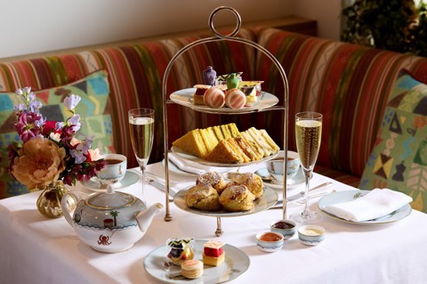 The Kit Kemp Design Thread Afternoon Tea set up at The Whitby Bar. There is a cake stand with scones, cakes decorated with Kit Kemps Famous fabrics, edible mannequins and sandwiches with tea and Champagne