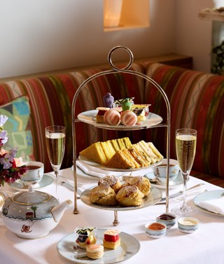 The Kit Kemp Design Thread Afternoon Tea set up at The Whitby Bar. There is a cake stand with scones, cakes decorated with Kit Kemps Famous fabrics, edible mannequins and sandwiches with tea and Champagne