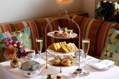 The Kit Kemp Design Thread Afternoon Tea set up at The Whitby Bar. There is a cake stand with scones, cakes decorated with Kit Kemps Famous fabrics, edible mannequins and sandwiches with tea and Champagne