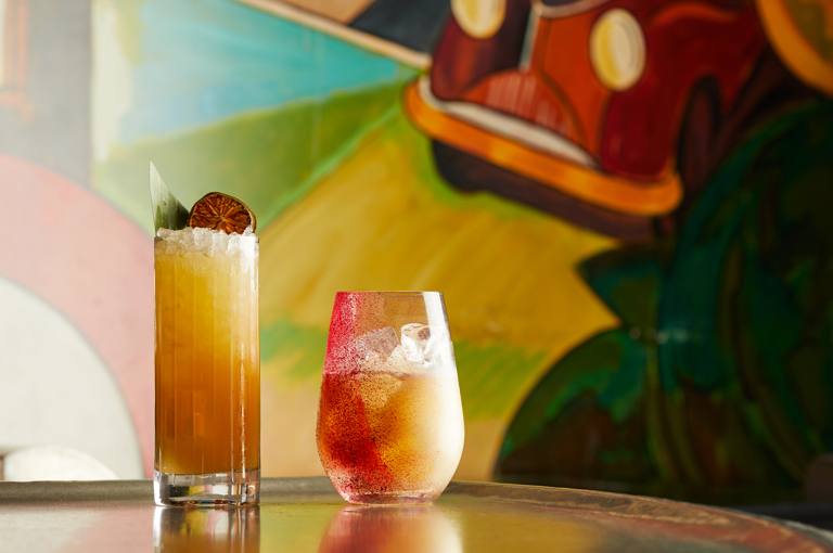 Wide shot of two cocktails placed on the bar in front of the art wall at Refuel