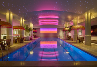 A wide shot looking down the swimming pool at Haymarket Hotel. There is a pink and orange light installation at the opposite end