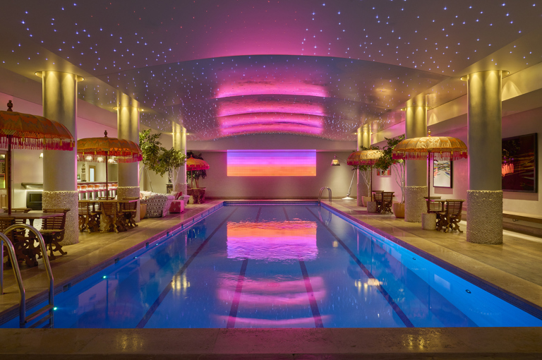 A wide shot looking down the swimming pool at Haymarket Hotel. There is a pink and orange light installation at the opposite end