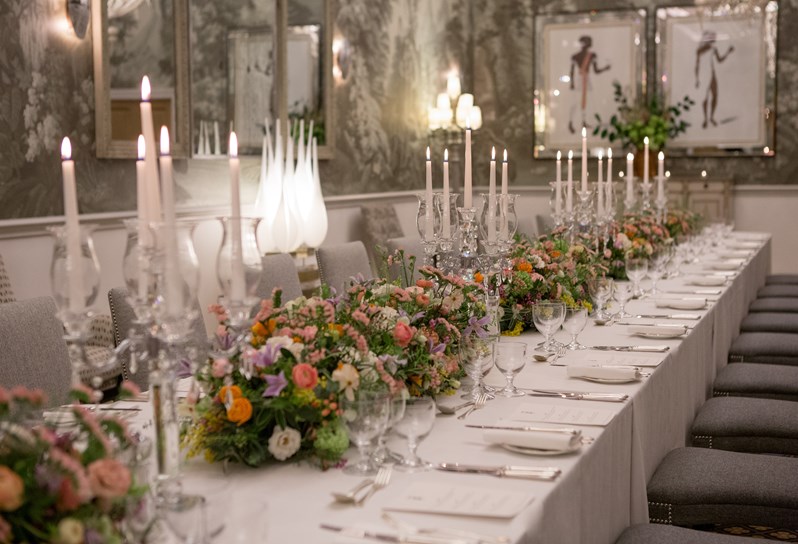 Shot down a long table dining set up in the Shooting Gallery at Haymarket Hotel. The table is dressed with colourful bouquets of flowers and long candle sticks.