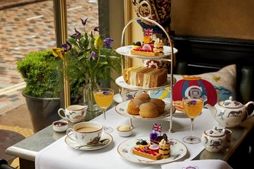 Afternoon tea displayed on a table in Brasserie Max restaurant at the Covent Garden Hotel. The fine bone china is Mythical Creatures by Kit Kemp for Wedgwood along side a 3 tier cake stand, sandwiches and scones.