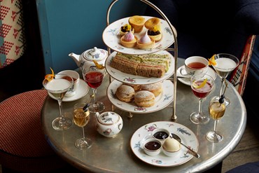 Champagne afternoon tea displayed on a table in Oscar restaurant at the Charlotte Street Hotel. The fine bone china is Mythical Creatures by Kit Kemp for Wedgwood along side a 3 tier cake stand, sandwiches and scones.
