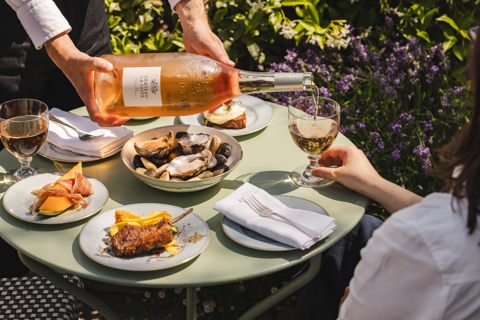 An image of a waiter pouring a bottle Chateau Le Coste with some dishes from the 'Rose on the Roof' menu at Ham Yard Hotel.
