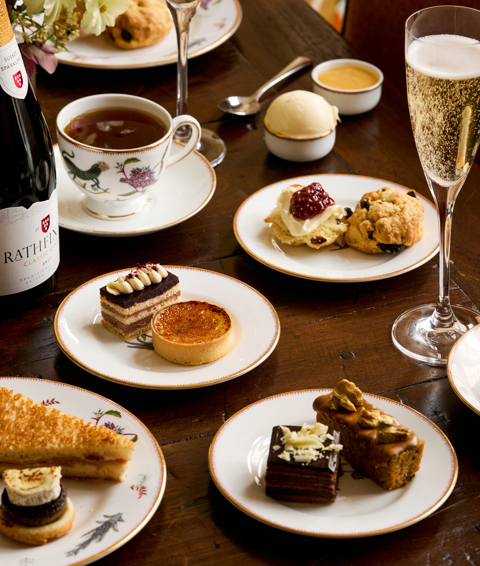 A portrait shot of the items in the Bloomsbury Set Afternoon Tea at Oscar: there are plates of pastries, cakes and sandwiches, served with a bottle of sparkling wine