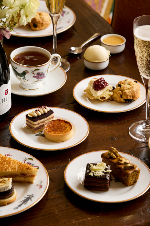 A portrait shot of the items in the Bloomsbury Set Afternoon Tea at Oscar: there are plates of pastries, cakes and sandwiches, served with a bottle of sparkling wine