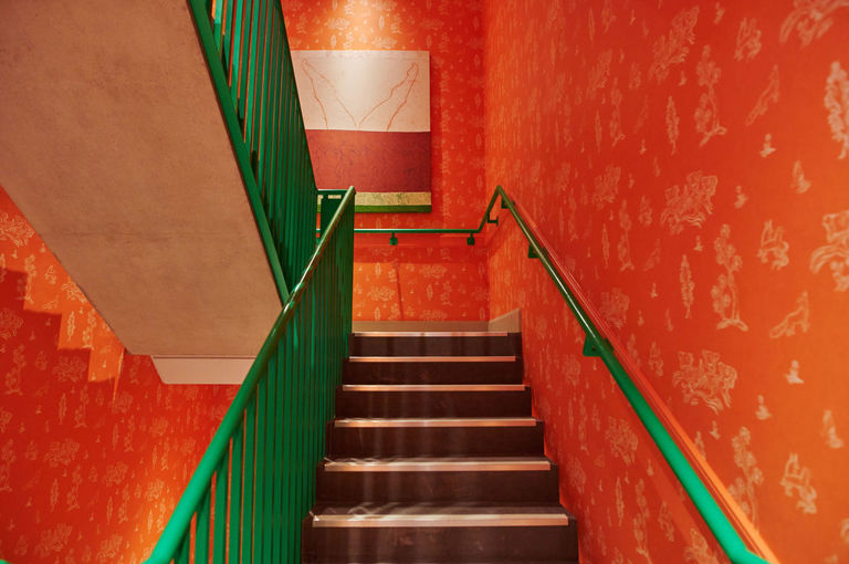 A wide shot of the colourful stairwell. The walls have been lined in Kit Kemp's Friendly Folk and the hand rail has been painted in a bright emerald green at 9-11 Richmond Buildings.