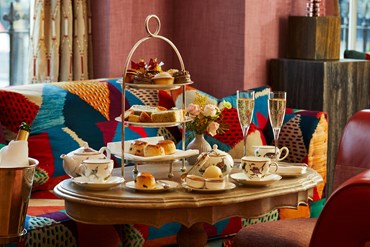 Champagne afternoon tea displayed on a table in Brumus restaurant at the Haymarket Hotel. The fine bone china is Mythical Creatures by Kit Kemp for Wedgwood along side a 3 tier cake stand, sandwiches and scones.