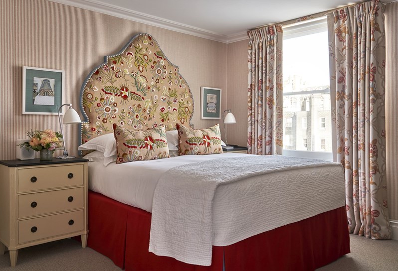 Diagonal bedroom shot of a luxury room with striped light coloured walls and colourful nature drawings on the pillows and headboard.