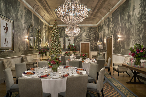 Shot of round dining festive tables and a Christmas tree in the Shooting Gallery at Haymarket Hotel. The tables displays dining set up with Mythical Creatures crockery, festive flower displays and crackers.