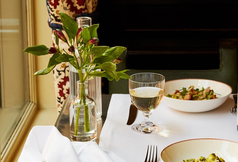 An image of a table with two main course dishes of Gnocchi in a bowl, at Brasserie Max restaurant at Covent Garden Hotel. The table also has a bottle and two glasses of wine. This image is to promote dining collaboration with The Producers theatre production.
