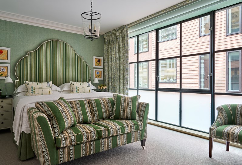 A room at Ham Yard Hotel with a large statement headboard in green stripes with a matching sofa at the end of the bed