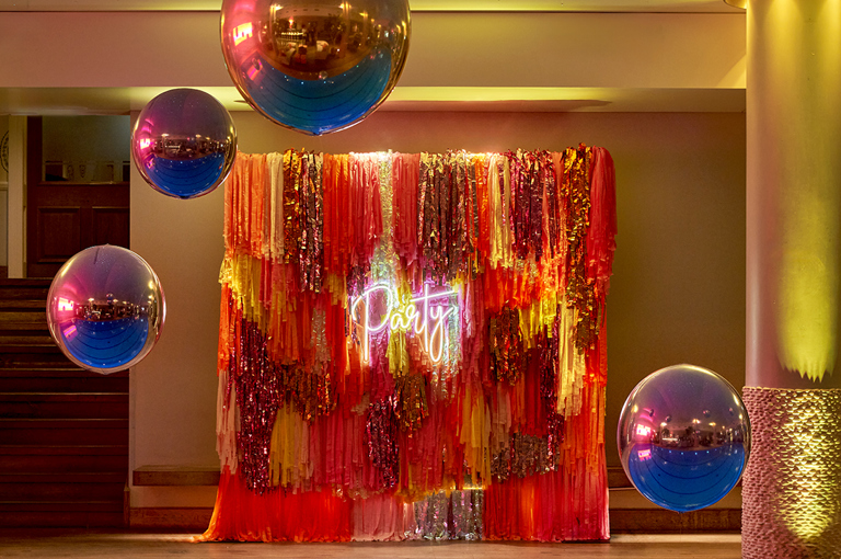 The pool at Haymarket Hotel decorated for a party with silver helium baloons floating over the water and a tasseled display which says 'party' in neon lights