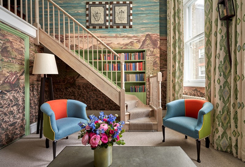 An image of two blue and red rub chairs in front of a wooden staircase and nautical wallpaper in the loft suite at Charlotte Street Hotel