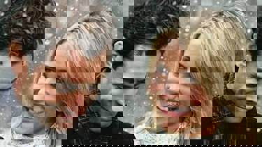 A still from 'The Holiday'. A close up a man and woman in the snow. The blonde woman looks to her right smiling at the man as he looks down smiling.