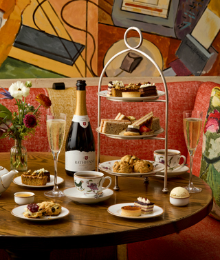 A portrait shot of the Bloomsbury Set Afternoon Tea at Oscar: There is one afternoon tea stand on the table next to a bottle of sparkling wine