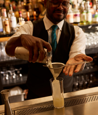 A bartender pours a cocktail through a small sieve into a glass at Warren Street Bar at Warren Street Hotel New York