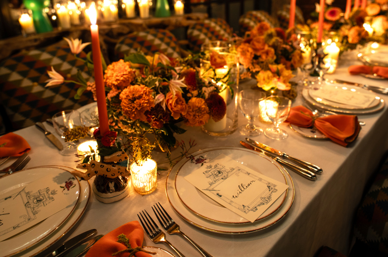 A close up image of a long table set up for dinner with dim candle lighting in The Orangery at Crosby Street Hotel.  