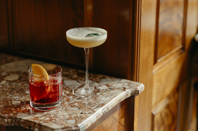A close up short of a negroni and martini cocktail on a marble surface in Brasserie Max