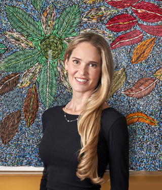 Willow Kemp stands in front of a piece of art work made up of small paper beads