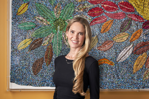 Willow Kemp stands in front of a piece of art work made up of small paper beads