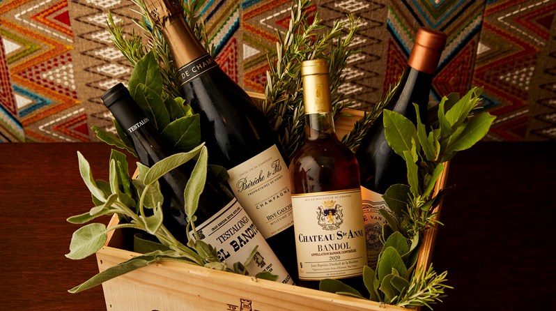 A wooden wine box filled with a selection of different wine bottles surrounded by herbs.