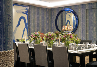 An image of the long dining table set up in the Indigo Room, there are floral bouquets in the centre and candles. each place around the table has a placemat, plate, cutlery, glassware and napkins ready for dining. private events room at The Soho Hotel.