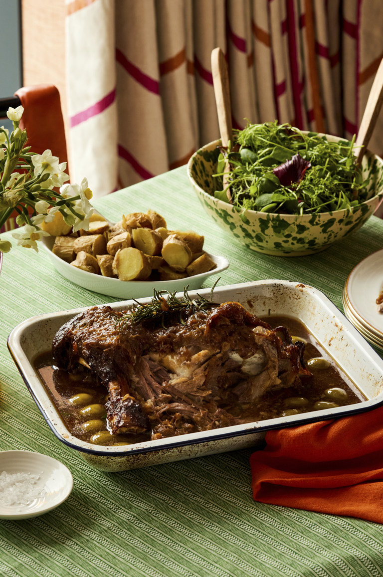 A portrait shot of a oven dish filled with slow cooked lamb. The lamb is accompanied by potatoes and salad