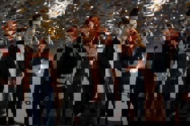 A still from the film Now You See Me, Now You Don't. A man dressed in a suit, is on the phone looking concerned. Behind him, two women and three men are seen out of focus, also looking concerned