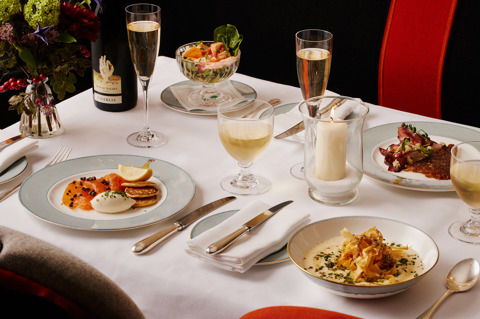 An image of the starters from the Christmas Day menu at Ham Yard Restaurant, Ham Yard Hotel. On the table, you can see Smoked salmon, caraway blinis, crème fraîche, capers and lemon, Dorset crab, native lobster and prawn cocktail, apple and horseradish, Roast parsnip, honey and truffle soup, parsnip crisps all on Sailor Fairwell crockery. Also on the table you can see glasses of wine and champagne and festive flowers.   