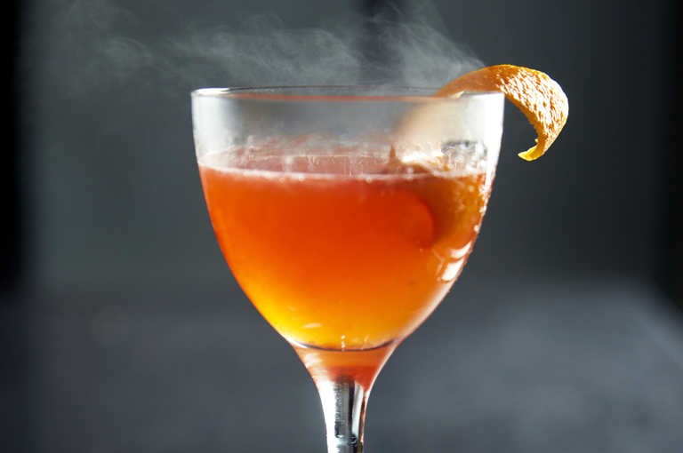 A close shot of a smoking orange cocktail at Ham Yard