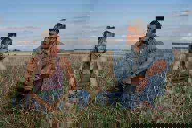 A still from the film "Reminders of Him" showing the two main characters sitting in a field. 