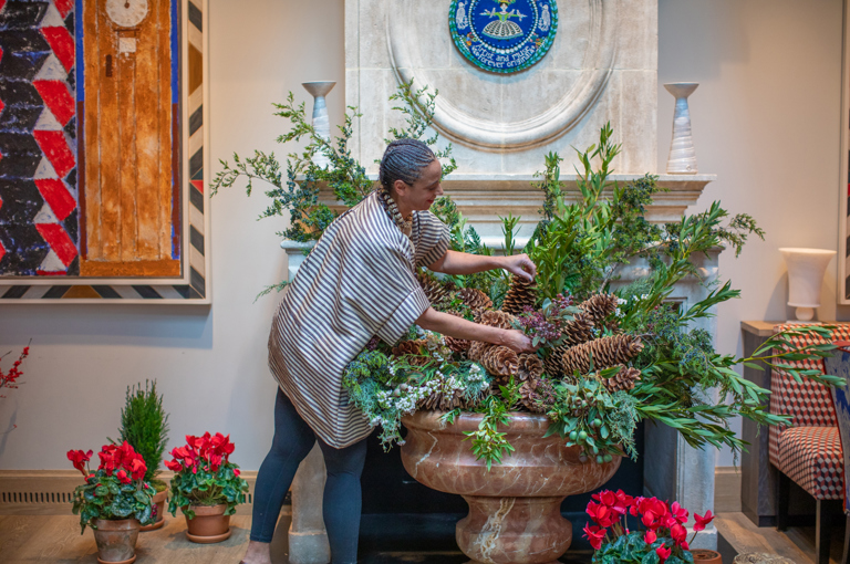 Florist Tawana Schlegel creating a winter foliage display in a large vase in front of a fireplace at Warren Street Hotel